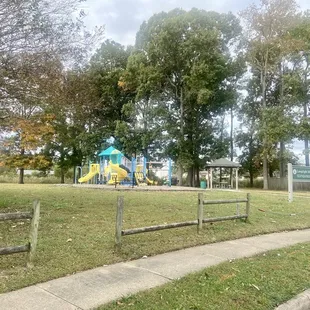 A view of Lamplight Manor Park (and its fence in need of mending and the sidewalk that separates it from the street)