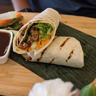 two burritos on a cutting board with dipping sauce