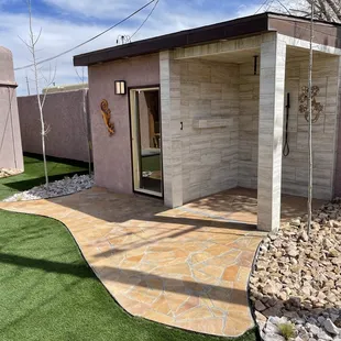 Outdoor sauna shower combo with flagstone landing, synthetic turf, aspen trees for minor shower privacy (photographed dormant), and cobble.