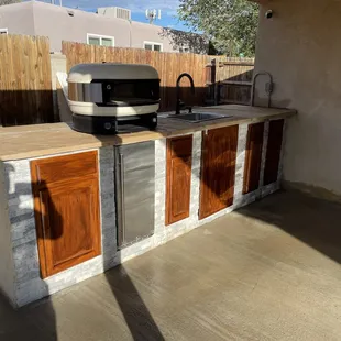 Simple outdoor kitchen with customer supplied Pizza cooker, plenty of cabinet space, a mini fridge and outdoor sink.