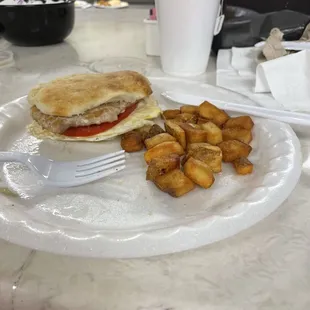 Tenderloin sandwich with fried egg and tomato with a side of fried potatoes.