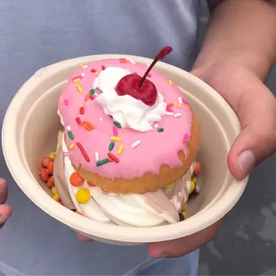 a pink frosted donut with sprinkles and a cherry on top