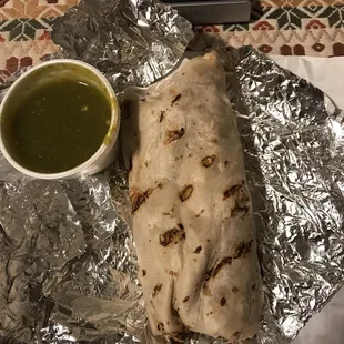 a burrito wrapped in tin foil with a bowl of salsa