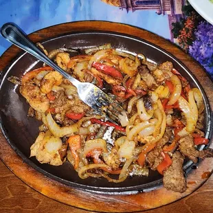 This is an uneaten plate of chicken and steak fajitas. It's full of onions and peppers.