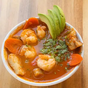 a bowl of soup with shrimp, carrots and avocado