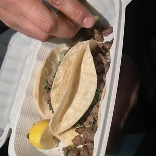 a hand holding a taco in a styrofoam container
