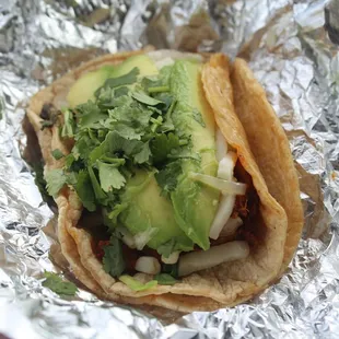 Corn taco with carnitas, cheese, avocado, cilantro and onions