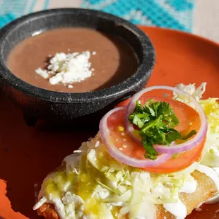Corn empanadas (meat/veggie) with crema, queso, cabbage, onions, tomatoes, and refried beans. Vegan option available (contains gluten).