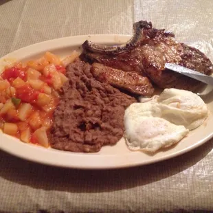 Pork Chop and eggs with a side of Papas a la Mexicana and Refried Beans.