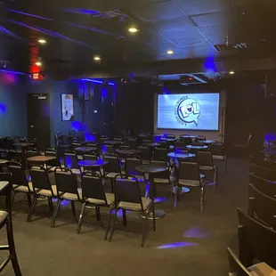 a large room with tables, chairs, and a projector screen