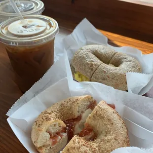 Sesame bagel with cream cheese and strawberry jelly; cinnamon raisin bagel with egg, bacon, and cheese in the back; iced coffee; mocha