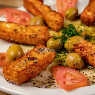 a plate of fried tofu with olives and tomatoes