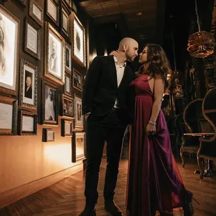 a man and a woman in formal attire standing in front of framed pictures