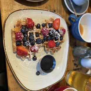 a plate of waffles with berries and powdered sugar