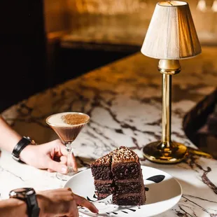 two people at a table with a piece of chocolate cake and a martini