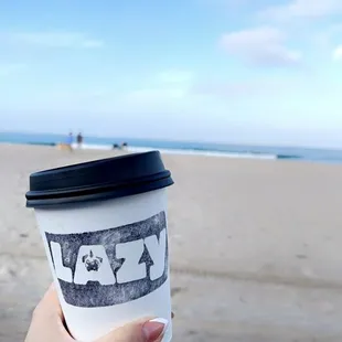 a hand holding a coffee cup on the beach