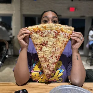 a woman holding up a slice of pizza