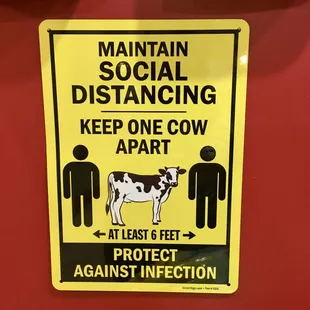 a sign stating social distancing keep one cow apart