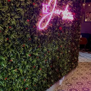 a plant wall with a neon sign