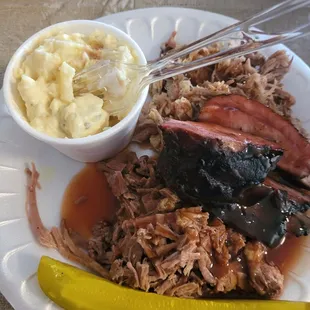 ows a plate of pulled pork, macaroni and cheese and a pickle