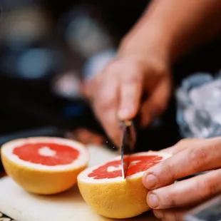 a person cutting grapefruit on a cutting board