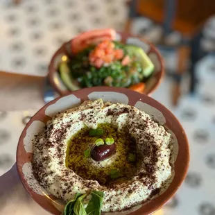 a hand holding a bowl of hummusle