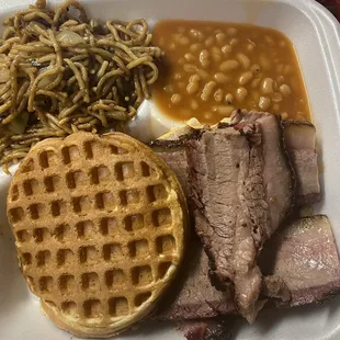 Sliced brisket on a waffle bun with garlic noodles and baked beans.