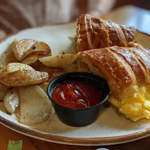 a croissant sandwich with eggs, potatoes and ketchup