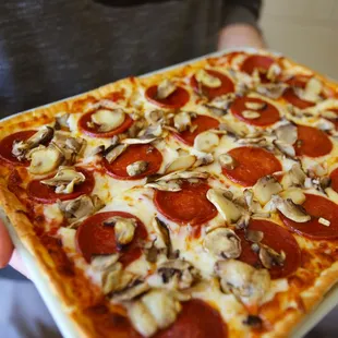 a person holding a square pizza