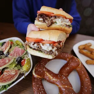 a person holding a sandwich over a salad and pretzels