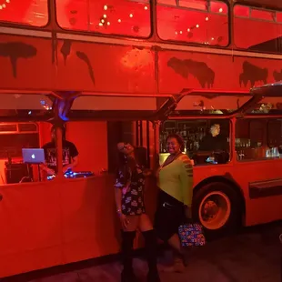 a red double decker bus parked in front of a bar