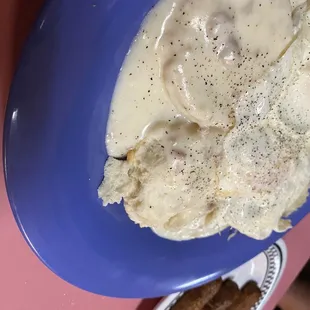 Biscuits and gravy with two eggs over easy on top and side of link sausage.