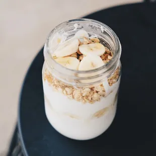 a glass of yogurt with bananas and granola