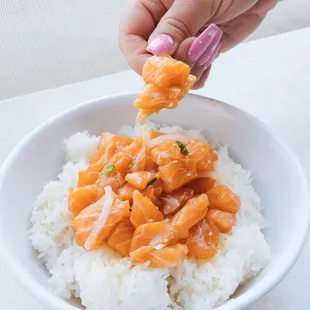 a hand holding a spoon over a bowl of rice