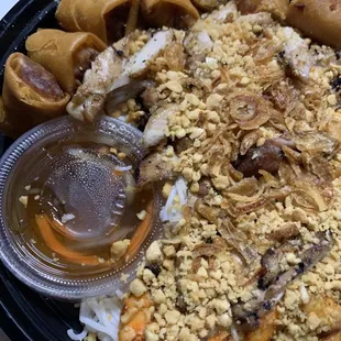 Shrimp and chicken with spring rolls over noodles with nuts on top.