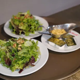 two plates of salad and a bowl of dressing