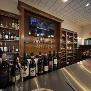 a woman behind a bar with bottles of wine