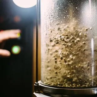 a hand pointing towards a blender filled with coffee beans