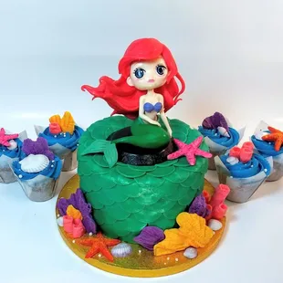 a little mermaid sitting on top of a cake