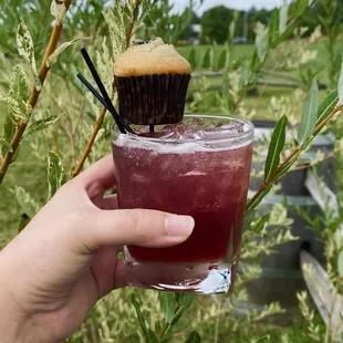 a hand holding a glass of wine with a cupcake on top
