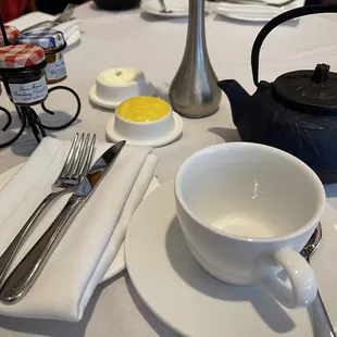 a table setting with a tea pot, teacup, spoon, and utensils