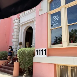 a woman sitting on the steps of a pink building