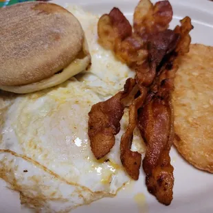 Two eggs over easy, crispy bacon, hash brown, and English muffin
