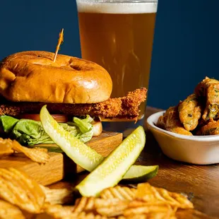 a chicken sandwich with pickles and a glass of beer