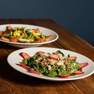 two plates of salad on a wooden table