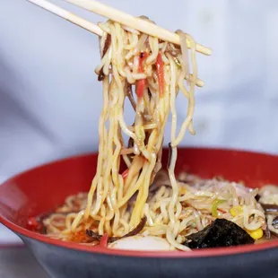 a person holding chopsticks over a bowl of noodles