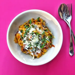 a bowl of pasta and a fork on a pink surface