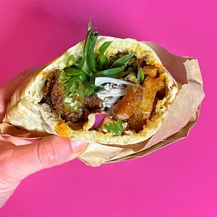 a hand holding a pita filled with meat and vegetables