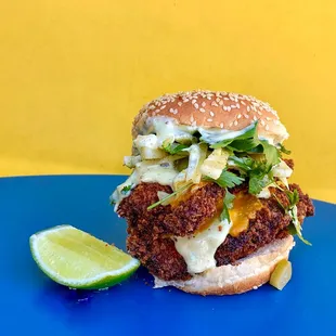 a fried chicken sandwich on a blue plate with a slice of lime