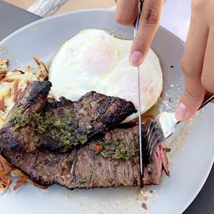 a person cutting a piece of steak with a knife and fork